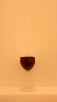 A glass of wine sitting on a table in front of a white wall photo