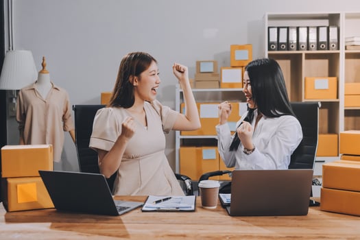 Two women sitting at a desk with laptops and boxes photo