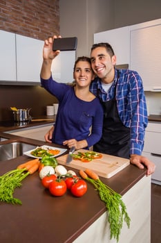 Couple in kitchen cooking and taking selfie with smartphone photo