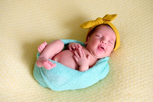 Close-up of a newborn baby girl smil, inside a ball of blue wool on a yellow blanket with a yellow bow on her heading photo