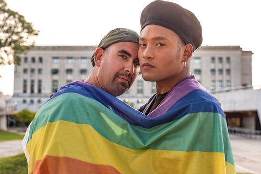 Gay couple under LGBT rainbow flag while looking at camera. Concept of Pride. Pride month. photo
