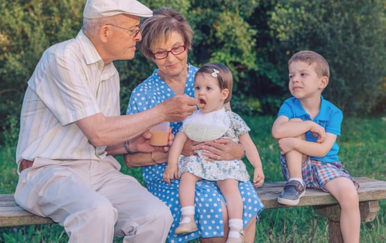 An older man and woman feeding a baby to an older child photo