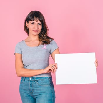 A yound woman wearing a pink breast cancer awareness ribbon holding a blank sign against a pink background photo
