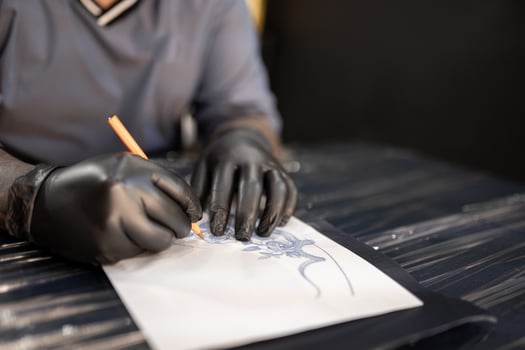 A tattoo artist is drawing a design stencil on his work stretcher before tattooing photo
