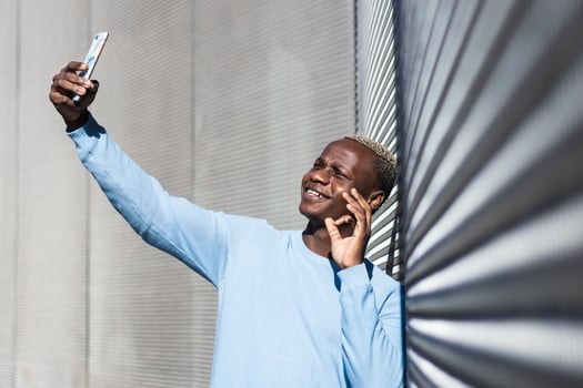 Cheerful young black guy doing OK sign while taking selfie on street photo