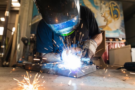 Welder in protective helmet welding metal detail in workshop photo