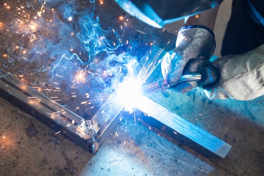 Welder in protective helmet welding metal detail in workshop photo