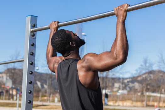 Unrecognizable strong black sportsman working out on bar in town photo