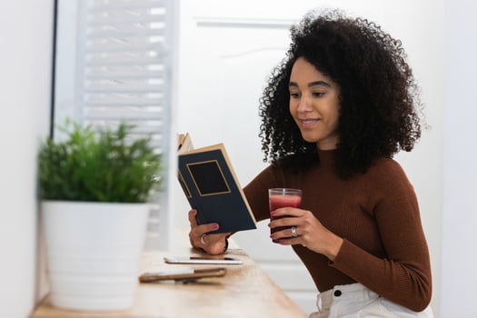 A woman with curly hair is holding a book and drinking a juice photo