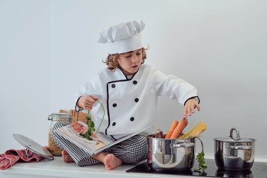 Positive boy sitting on counter and putting vegetables into sauc photo