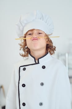 Amusing boy in chef uniform imitating mustache with spaghetti st photo