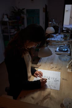 Female master painting jewelry sketches in dark workshop photo