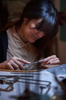 Attentive ethnic craftswoman using flat file while creating jewe photo
