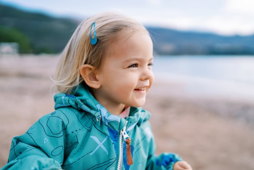 Little smiling girl stands on the beach and looks away photo