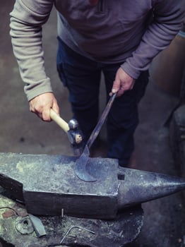 Crop anonymous master using hammer while forging metal on anvil photo
