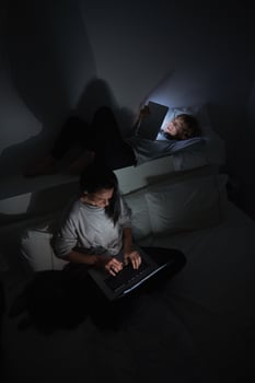 Woman and boy surfing gadgets in dark room at home photo