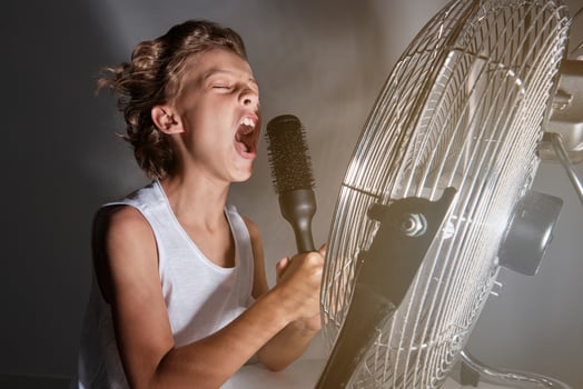 Boy singing into comb in front of working fan photo