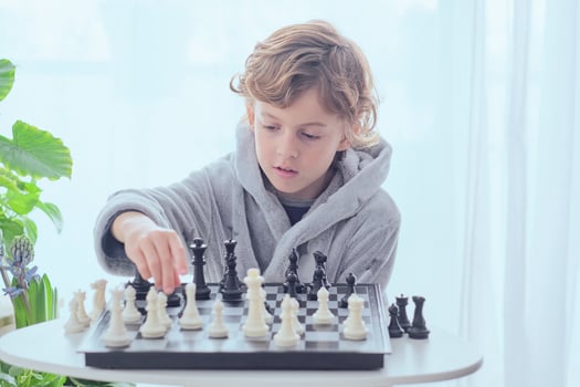 Focused preteen boy sitting at table and playing chess photo
