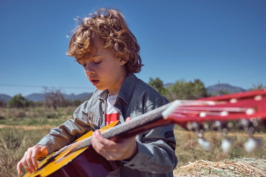 Little boy playing acoustic guitar on sunny day in countryside photo