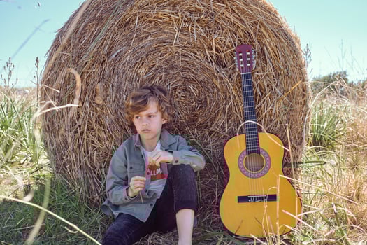 Upset kid sitting near guitar and leaning on hay bale photo