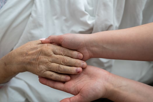 A young womans hands gently hold the hands of an elderly female patient in a hospital bed, symbolizing care, support, and compassion. photo