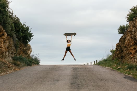 Joyful ethnic woman jumping high with longboard photo