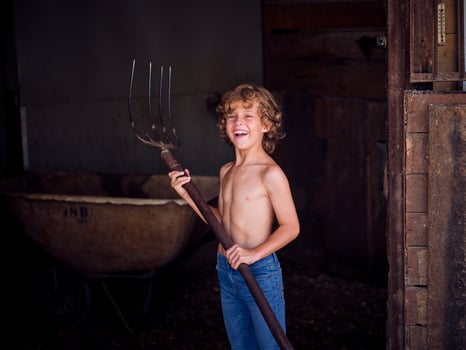 Cheerful kid with pitchfork standing in barn photo