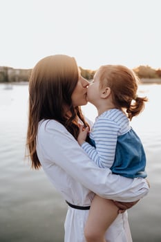A woman kisses her daughter on the cheek while standing by the water photo