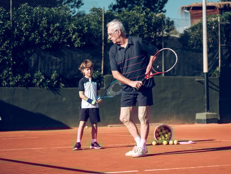 Senior tennis instructor teaching preteen boy on hard court photo