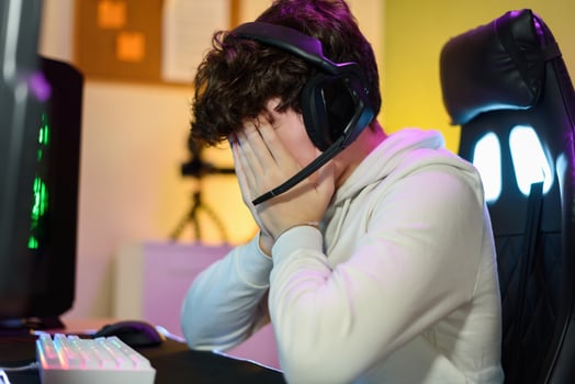 Anonymous young man sitting and covering face with hands near gaming PC photo