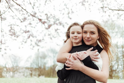 A woman and her daughter hugging in front of a tree photo