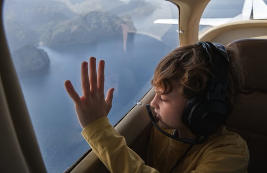 Curious boy looking out airplane window flying above sea photo