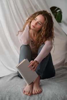 Portrait of young woman sitting on bed and holding book photo