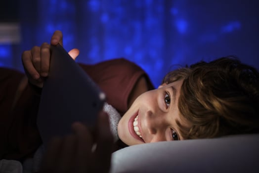 Cheerful boy with tablet lying on bed at night photo