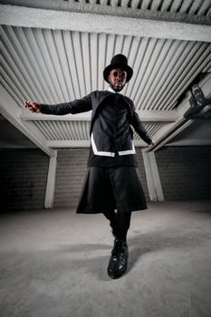 Stylish ethnic man in round sunglasses and hat standing in under photo