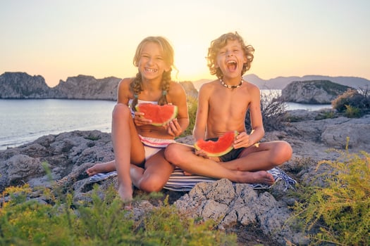 Laughing brother and sister enjoying watermelon on seashore photo