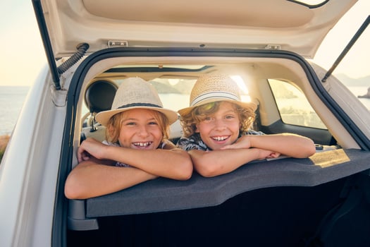 Two smiling children in straw hats leaning in the back seats of photo
