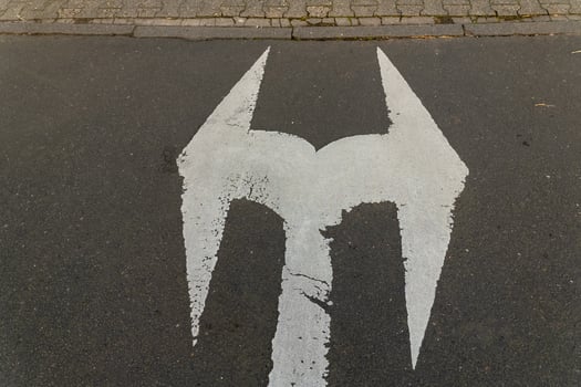 White marking resembling a logo on asphalt near a brick sidewalk in an urban setting photo