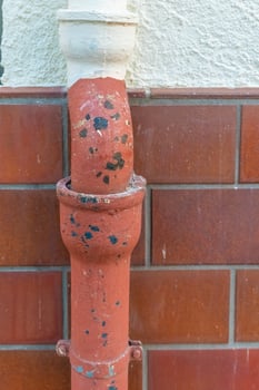 Rusty water pipe with chipped paint against tiled wall in urban setting under evening light photo
