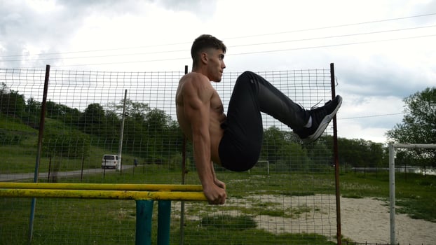 Strong guy training abdominal muscles on parallel bars at sports ground. Young shirtless sportsman exercising at nature. Sporty athlete working out at nature. Concept of active sportive lifestyle photo