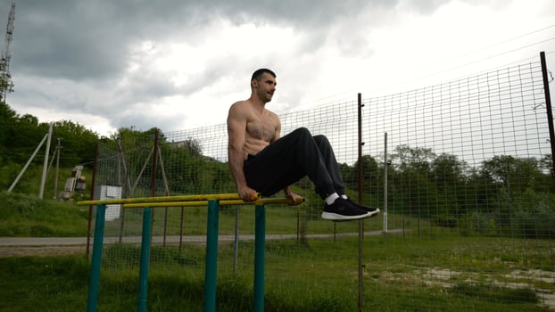 Strong guy training abdominal muscles on parallel bars at sports ground. Young shirtless sportsman exercising at nature. Sporty athlete working out at nature. Concept of active sportive lifestyle. photo