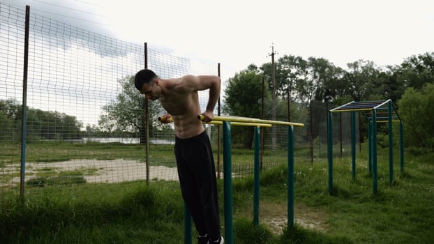 Young sportsman doing push ups on parallel bars at nature. Strong sporty man exercising at sports ground. Male shirtless athlete training hard outdoor. Concept of active sportive lifestyle. photo