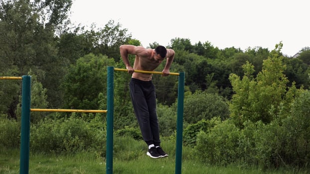 Hardy shirtless sportsman doing push ups on horizontal bar at nature. Strong and muscular guy training at sports ground. Young athletic guy exercising outdoor. Concept of active and healthy lifestyle. photo