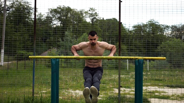Hardy shirtless sportsman doing exercises on parallel bars at nature. Strong and muscular man working out at sports ground. Young athletic guy exercising outdoor. Concept of active healthy lifestyle photo