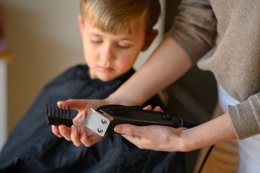 A barber shows a young boy the hair clipper, letting him touch it to ease his fear. photo