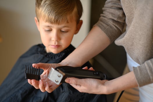 A stylist reassures a little boy by letting him hold and explore the hair clipper. photo