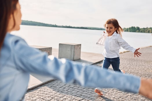 Little girl is running to the woman to embrace her. Young mother with her daughter having fun outdoors near the lake at summer photo