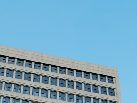 Modern skyscraper corner with geometric stone and glass design, under a bright blue sky. photo