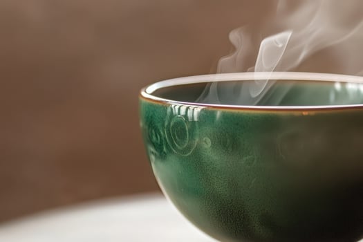 A green ceramic bowl emits steam, suggesting a freshly poured hot beverage inside. The bowls smooth surface reflects light, creating a cozy and inviting atmosphere. photo