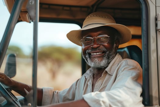 Black elderly man ranger in beige linen shirt sitting in SUV car near window, open top vehicle during African safari, adventure, spirit of freedom photo